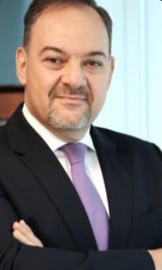 Middle-aged man with a goatee in a dark suit, arms crossed.