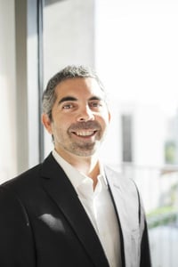 Graying man in a dark suit smiling near a bright office window.