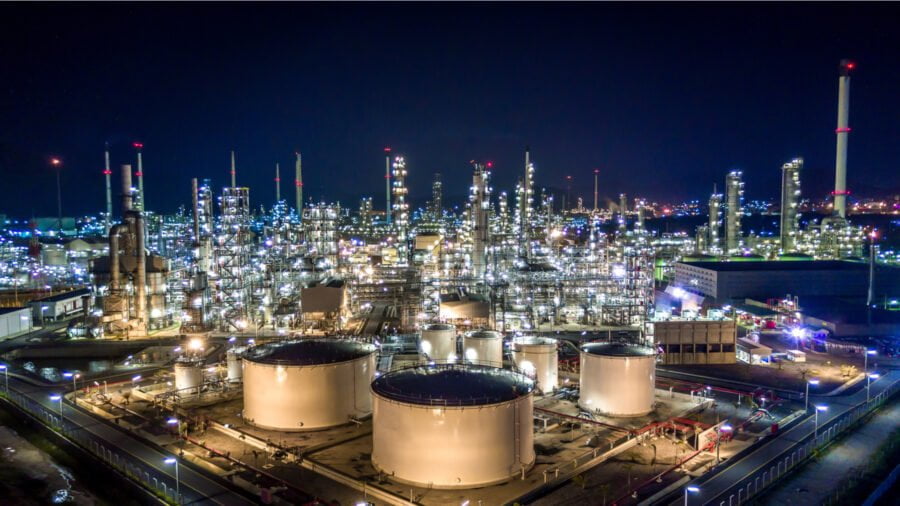 Large storage tanks in a brightly lit refinery complex at night.