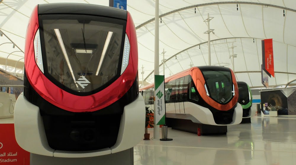 Red metro train with "Riyadh Metro" banner inside a modern station.