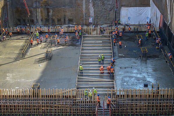 Workers pour concrete at large excavated construction site.