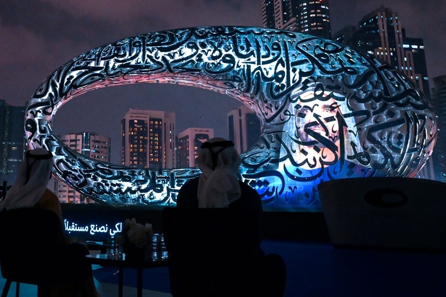 Arab figures observe calligraphic sculpture at night.