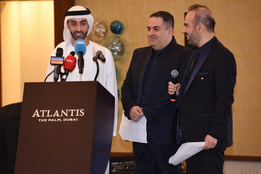 Man in traditional Emirati attire speaking at a podium.