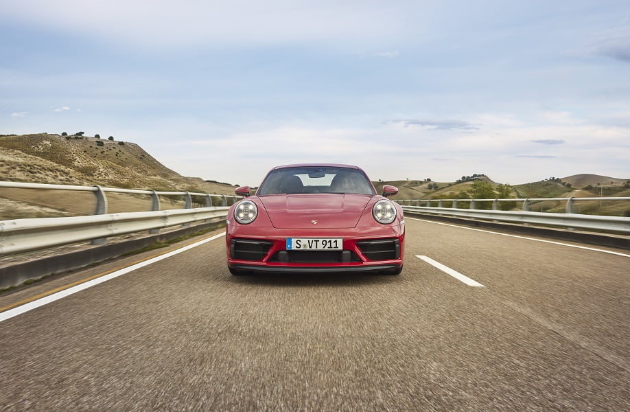 Red Porsche 911 driving on a highway with rolling hills in the background.