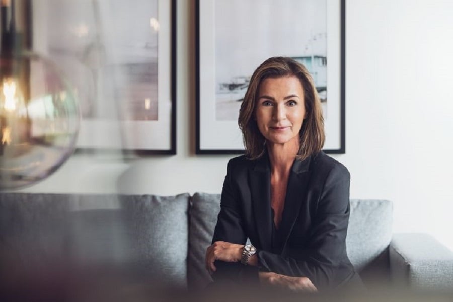 Woman in a black blazer posing on a gray couch with artwork on the wall.