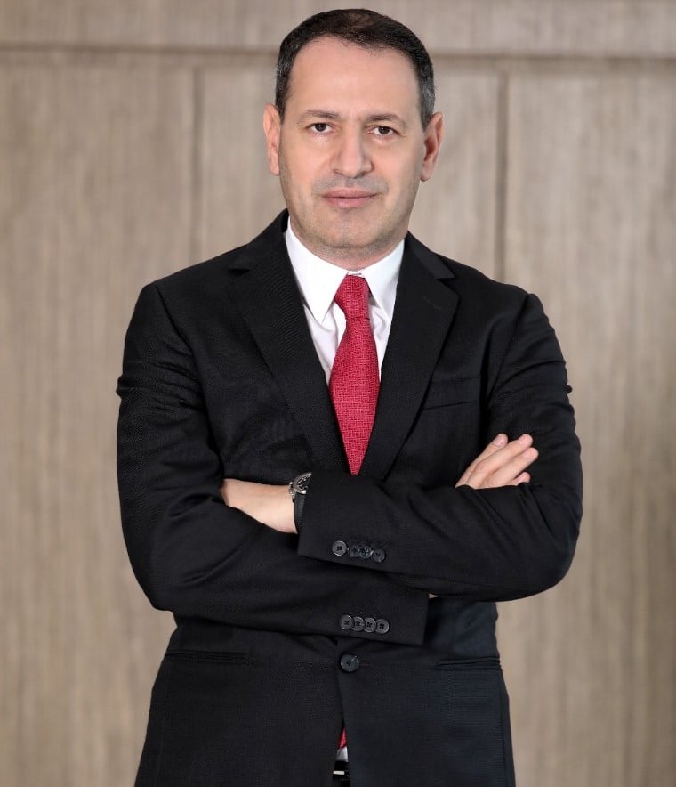 Man in suit standing with arms crossed against wood wall.