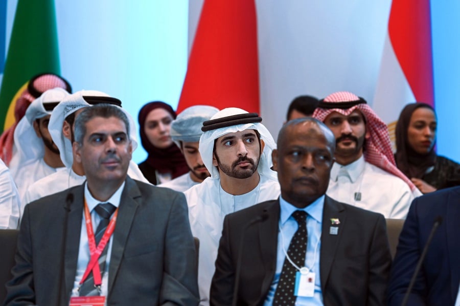 Emirati man sits at a conference with national flags in the background.