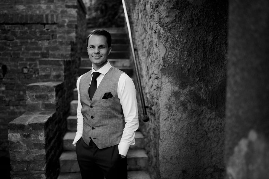 Man in vest and shirt stands by stone staircase.