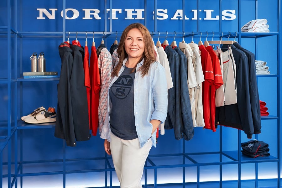A woman smiles in front of a clothing rack displaying North Sails apparel.