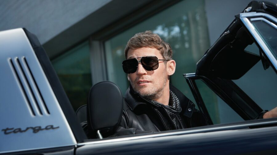 Man in sunglasses driving a classic Porsche Targa convertible.