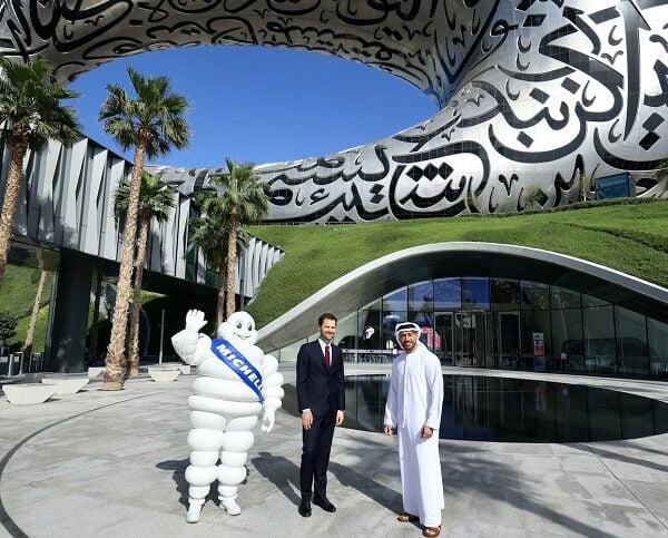 The Michelin Man waves near two men in business attire outside a building.
