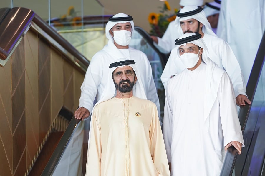 A man in a beige thobe descends an escalator with others in masks.