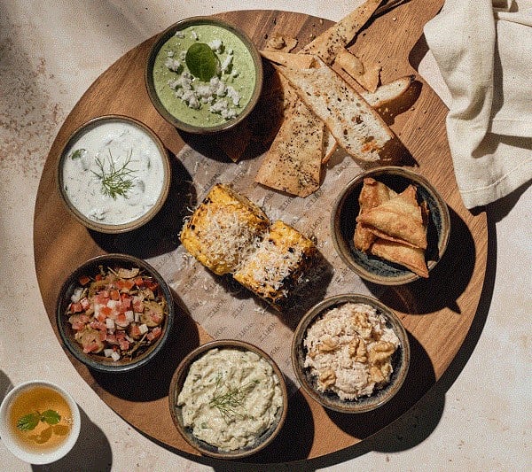 Assorted dips, snacks, and flatbreads on a wooden board.