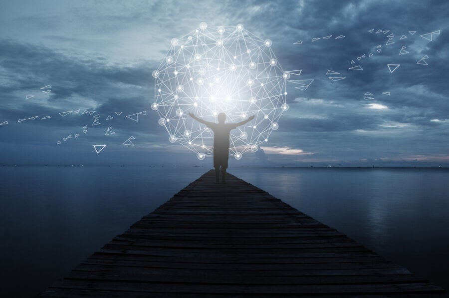 Person standing on a pier embracing a glowing network sphere.