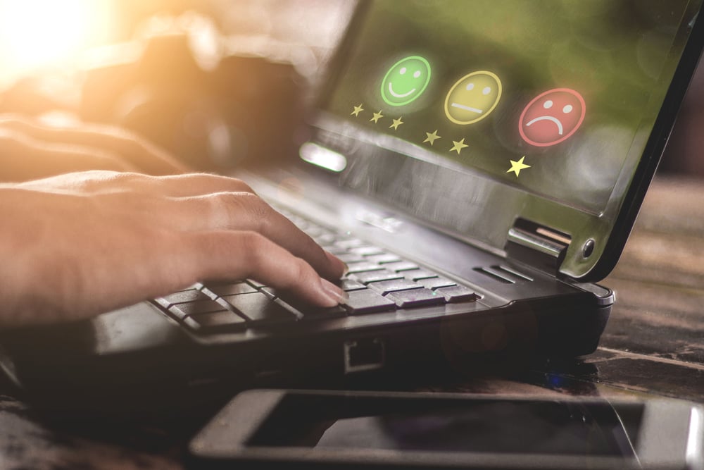 Hands typing on a laptop displaying emoticon rating options.