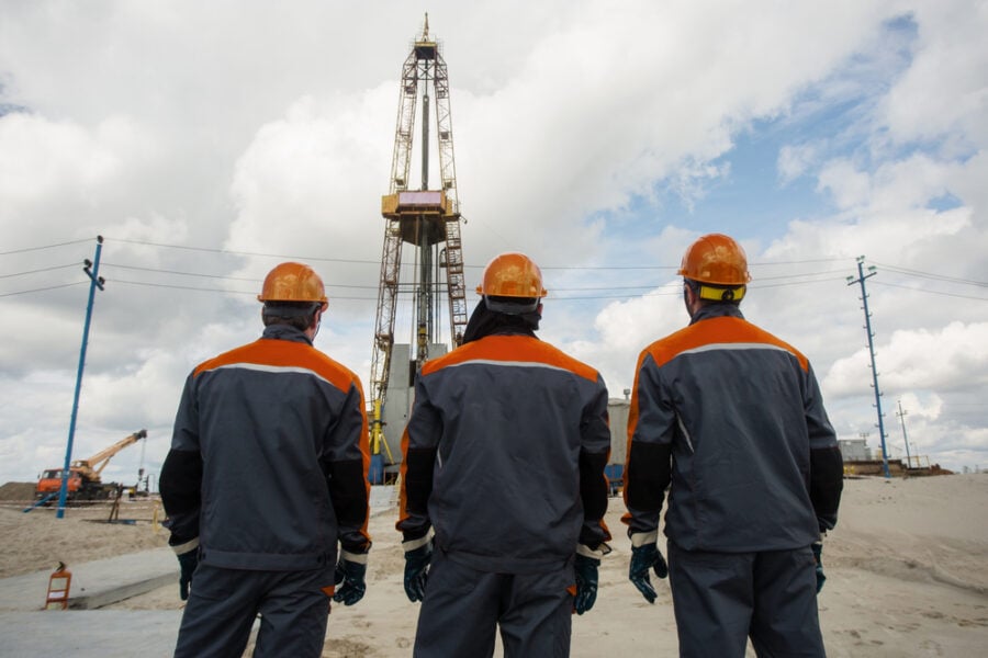 Workers near oil derrick in sandy landscape.