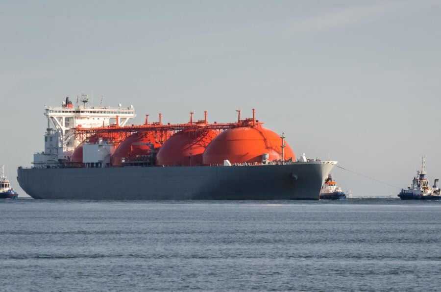 LNG carrier with orange tanks on a calm sea, assisted by tugboats.