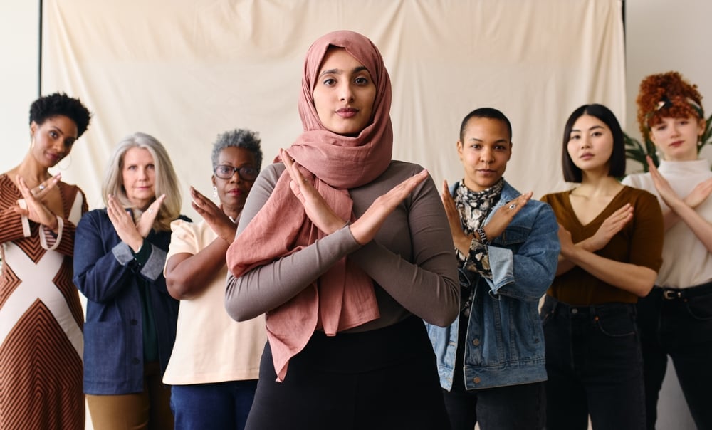 Woman in hijab making an "X" gesture with arms in a light room.