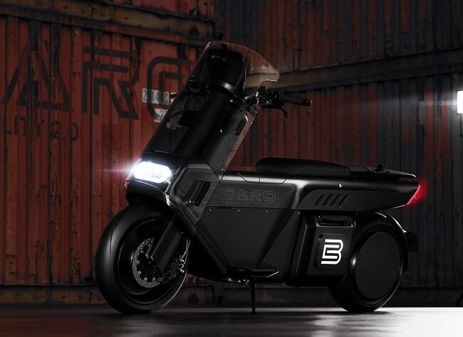 Black BARQ MOTORCYCLES scooter parked in front of rusty shipping containers.