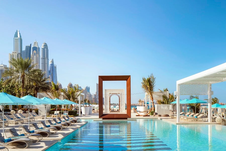 Resort pool with lounge chairs and umbrellas near city skyline.