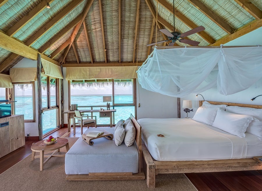 Bed in tropical overwater bungalow with ocean view.