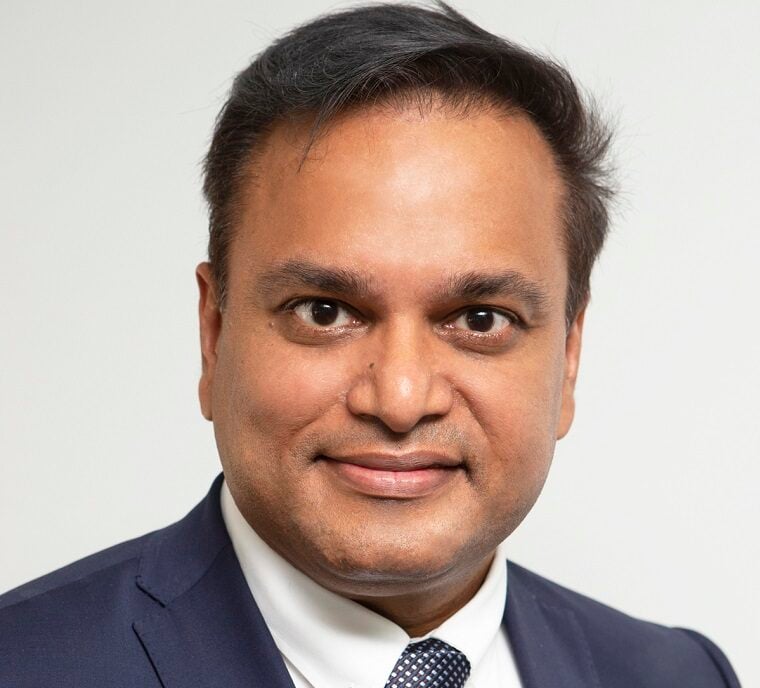 Man in dark suit posing against gray background.