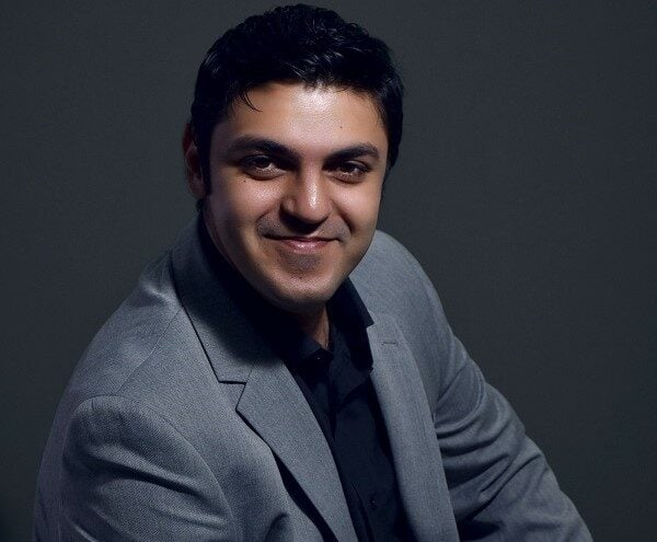 Man in gray suit smiling against a dark gray backdrop.