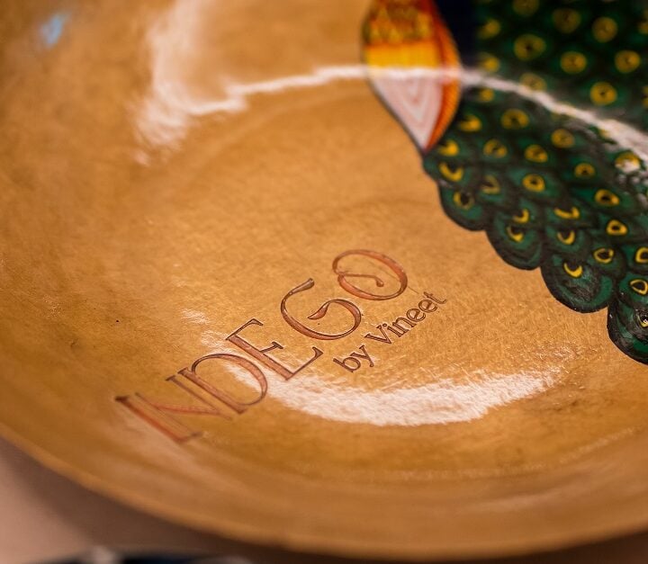Round plate with a peacock design and "INDIGO by Vineet" text.