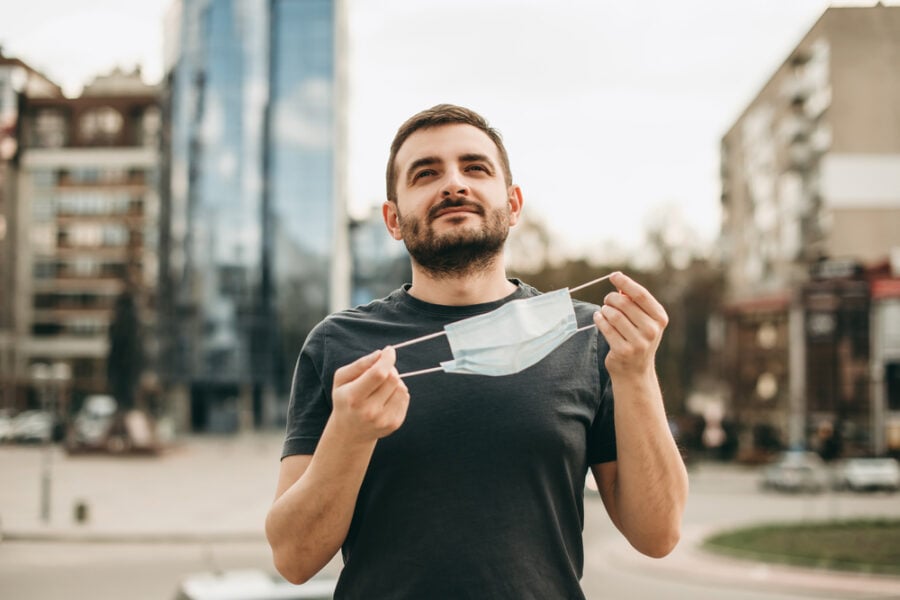 Man holding face mask looking upward in city.