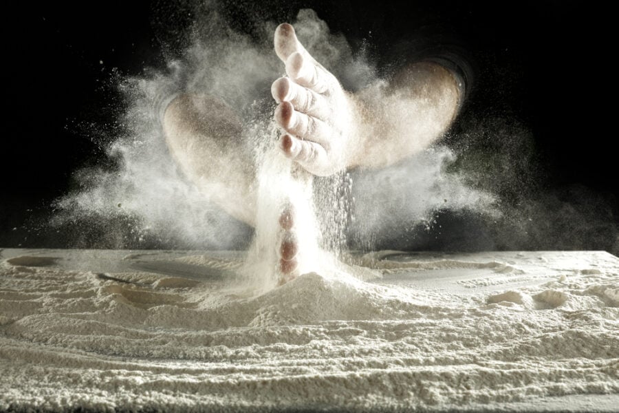 Hands clapping flour, creating a cloud on a dark surface.