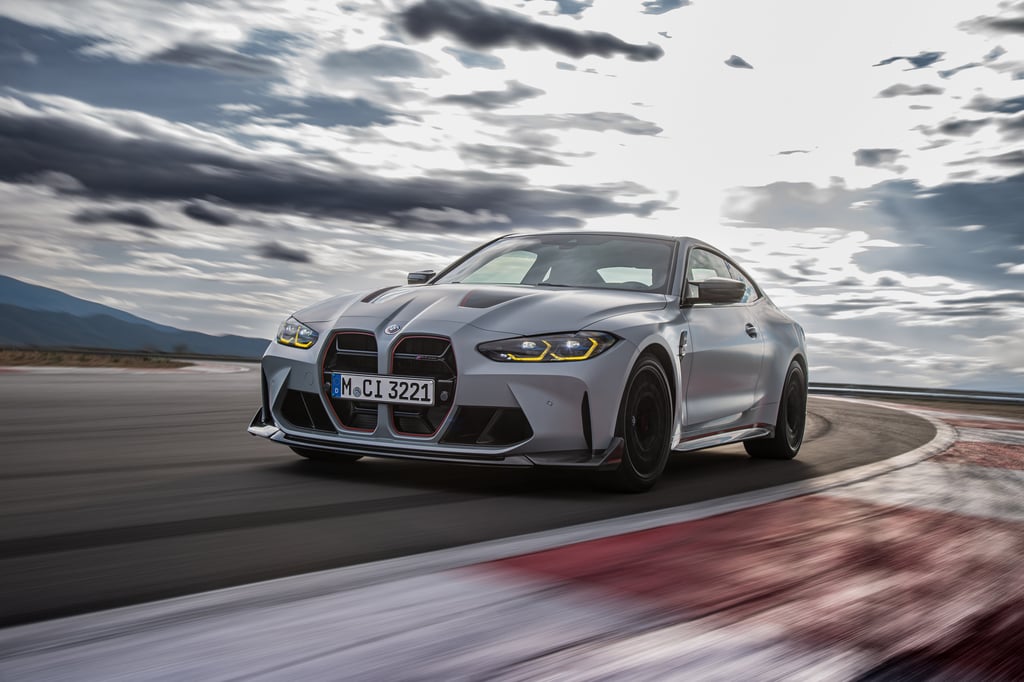 Silver BMW M4 drives on a racetrack under cloudy skies.