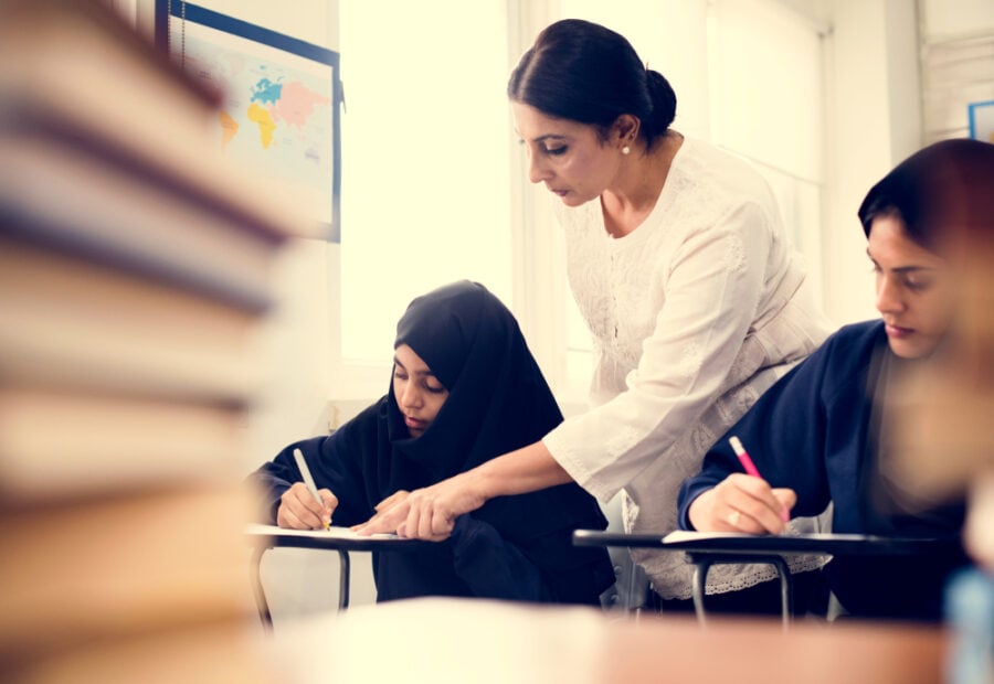 Teacher assisting veiled students writing in a classroom.