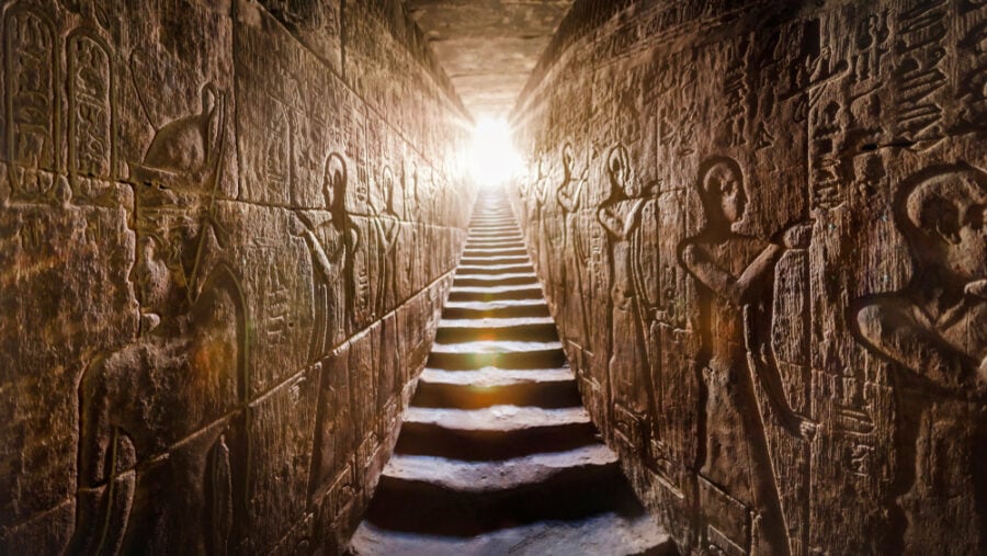 Stone stairs with Egyptian carvings leading to a bright light.