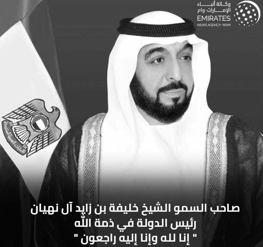 Black-and-white photo of Emirati man near flag.