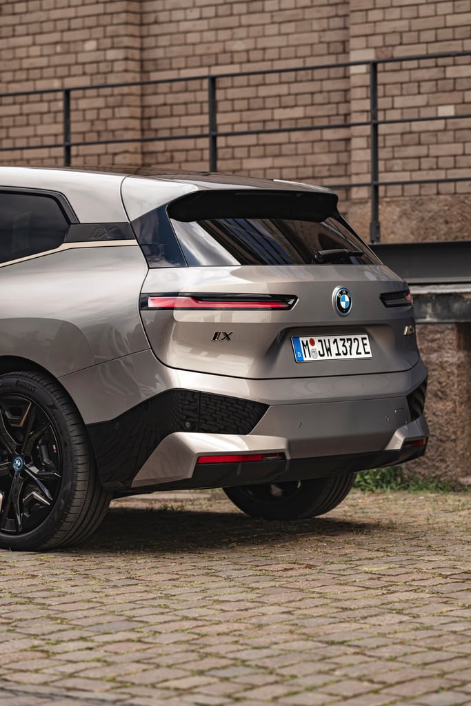 Silver BMW iX on cobblestones near a brick wall.