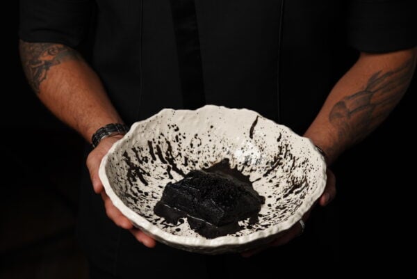 Person holding textured bowl with dark-colored food in dark setting.