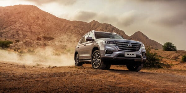 Silver SUV driving on a dirt road in a mountainous desert landscape.