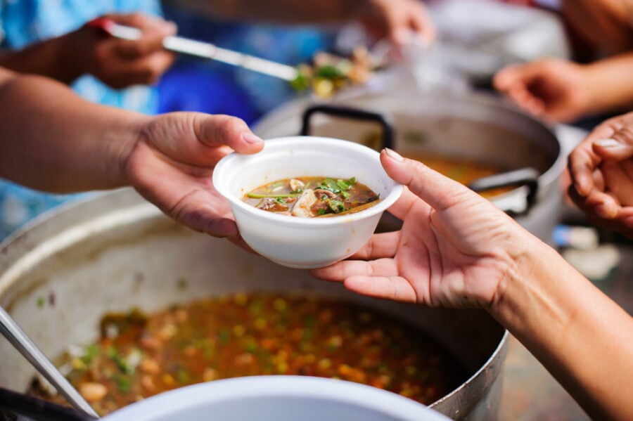 A bowl of stew is handed to a person in an outdoor food distribution.
