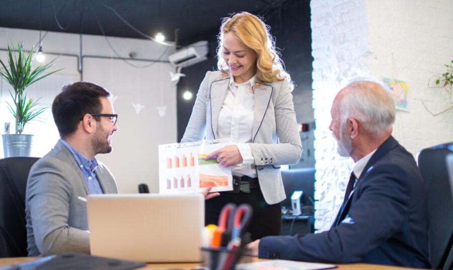 Woman presenting chart to colleagues in a modern office.