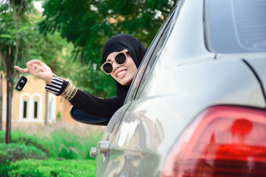 Woman in hijab shows car keys, smiling.