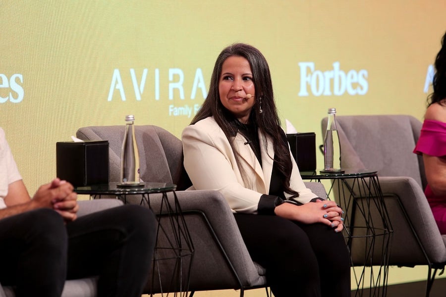 Woman on a panel discussion stage with logos visible.