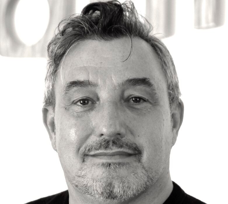 Man with wavy hair and a goatee gazing ahead against a bright background.