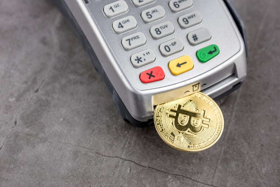 A Bitcoin coin enters a payment terminal's card reader.