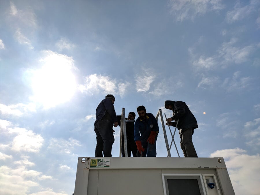 Workers install metal framework atop shipping container.