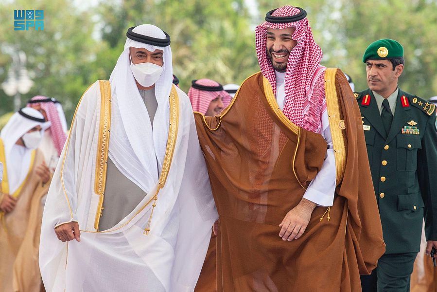 Two men in traditional attire walking outdoors with military officer.