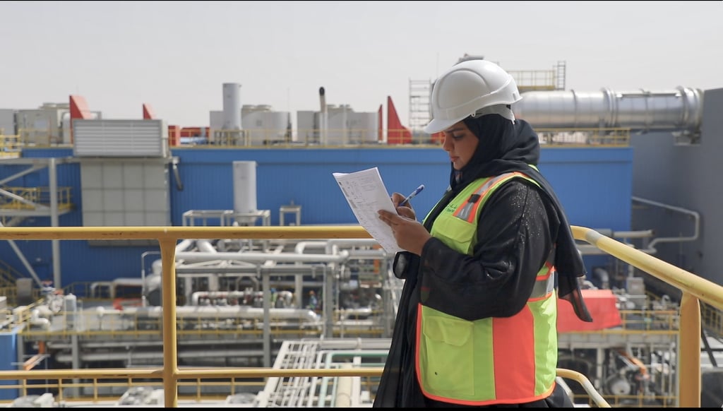 Woman in safety gear reviews paperwork at an industrial site.