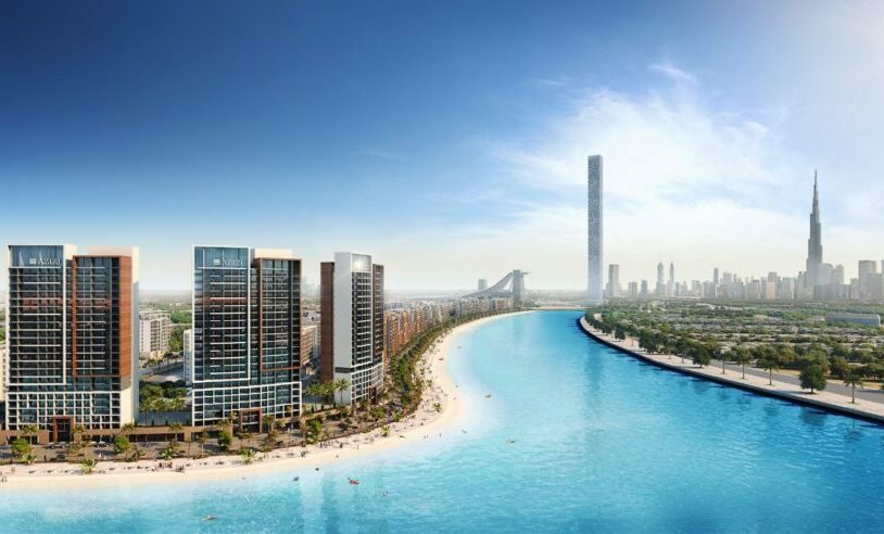 Apartment buildings by a sandy beach with a city skyline in the background.