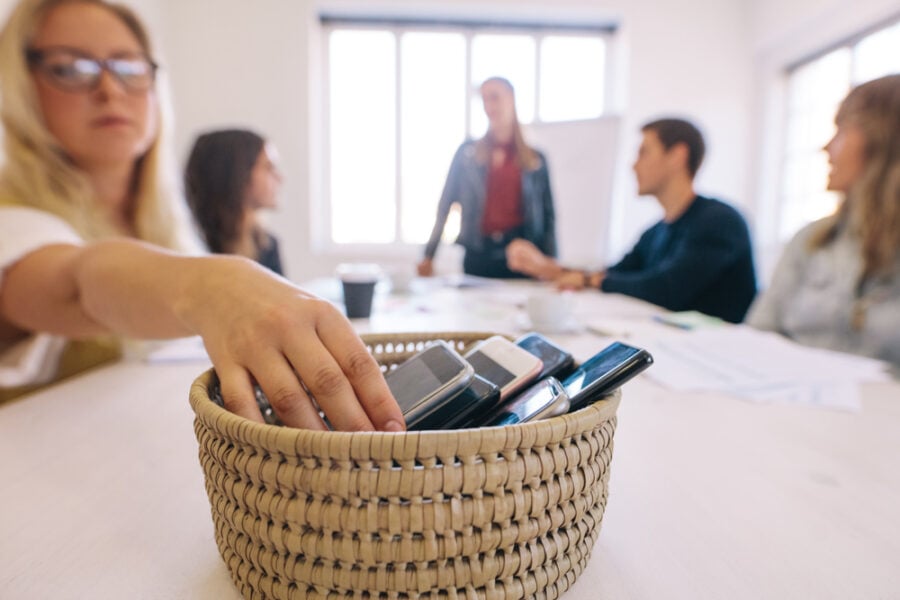 Hand places cell phones into basket on table at meeting.