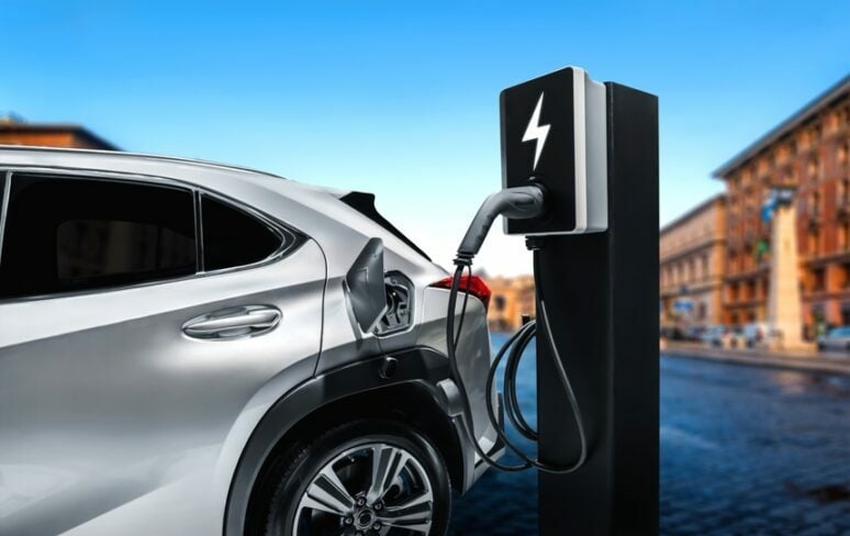 Silver SUV charging at an EV station in a city.