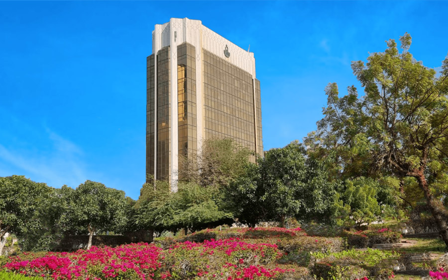 Golden-glass building surrounded by trees and flowers under a clear sky.